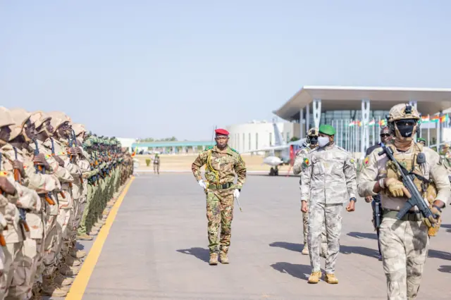 General Assimi Goita, Mali's transitional president in military uniform and green beret with a face covering, reviews troops.
