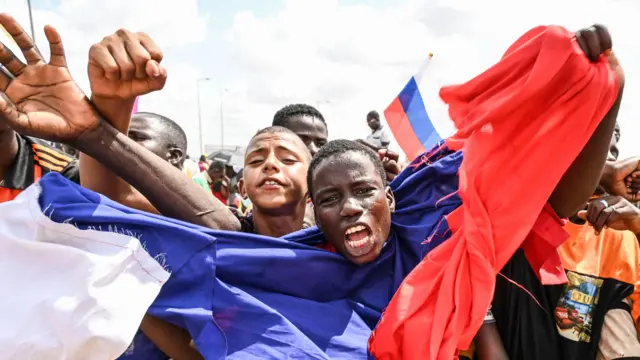 A man wrapped in a Russian flag waves and shouts as supporters of Niger's military leaders gather for a protest outside Nigerien and French air bases in Niamey on August 27, 2023.